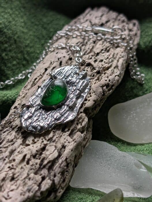 A high-texture fine silver pendant featuring deep, organic wood-grain patterns cast from real driftwood, holding a translucent green sea glass stone