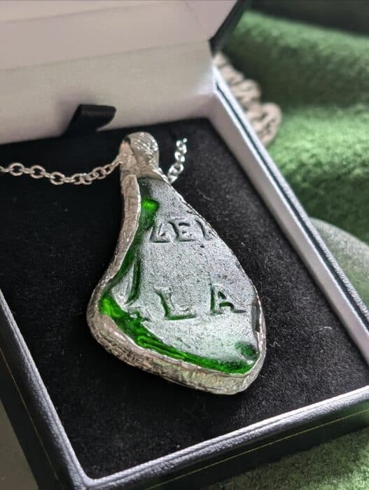 A triangular piece of frosted green sea glass with raised embossed letters 